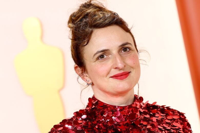 A brunette woman is pictured, shoulders up, wearing a red sequin dress and bright red lipstick.