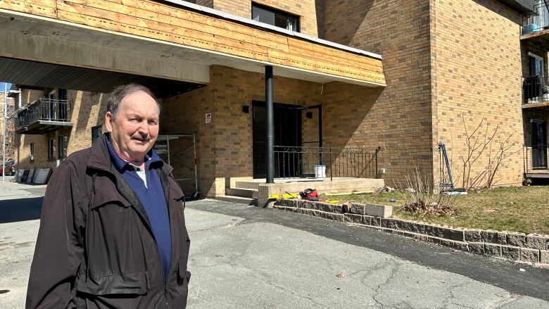 A man stands in front of a building as construction goes on behind him.