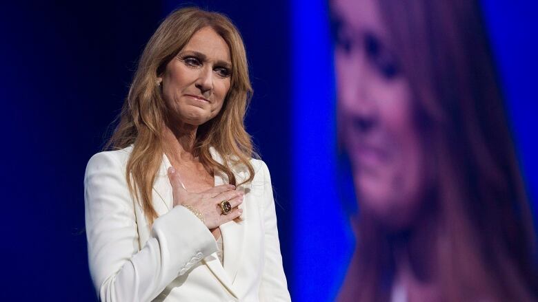 A woman wearing a white blazer places her hand over her heart.