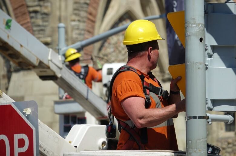 Two men in orange construction gear work on traffic lights.