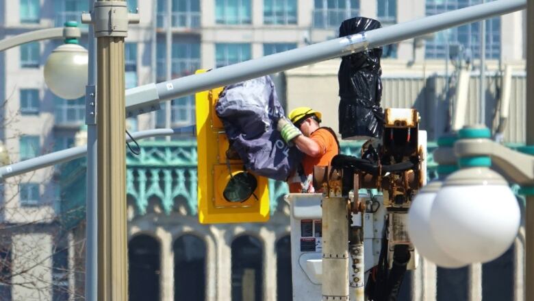 A man in orange construction gear puts a tarp on a traffic light.