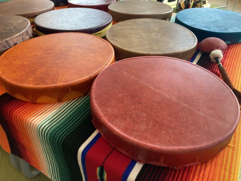 A variety of colorful round drums are laid out on a table covered with a blanket.