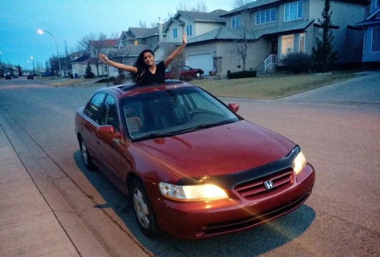 woman posing out of the sun roof of a red car.