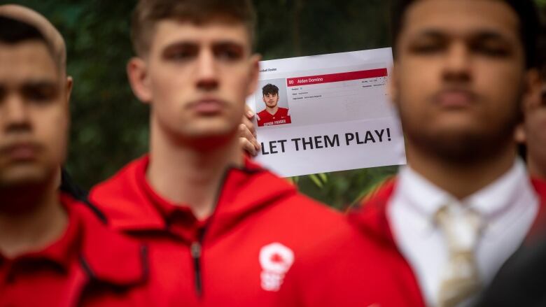 People in red shirts are pictured at a rally with a placard behind them reading 'Let them play!'