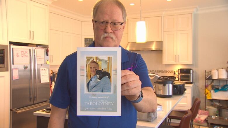 A man stands in his ktichen holding up a photo of his son.