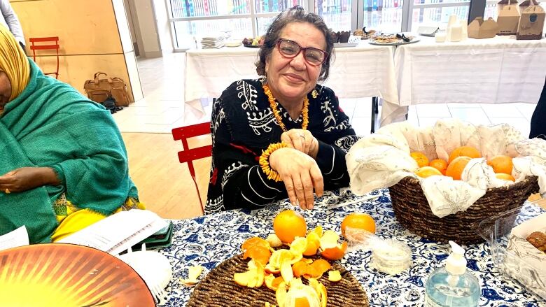 A woman holds out her hand to show a bracelet made of orange peels on a table with orange peels. 