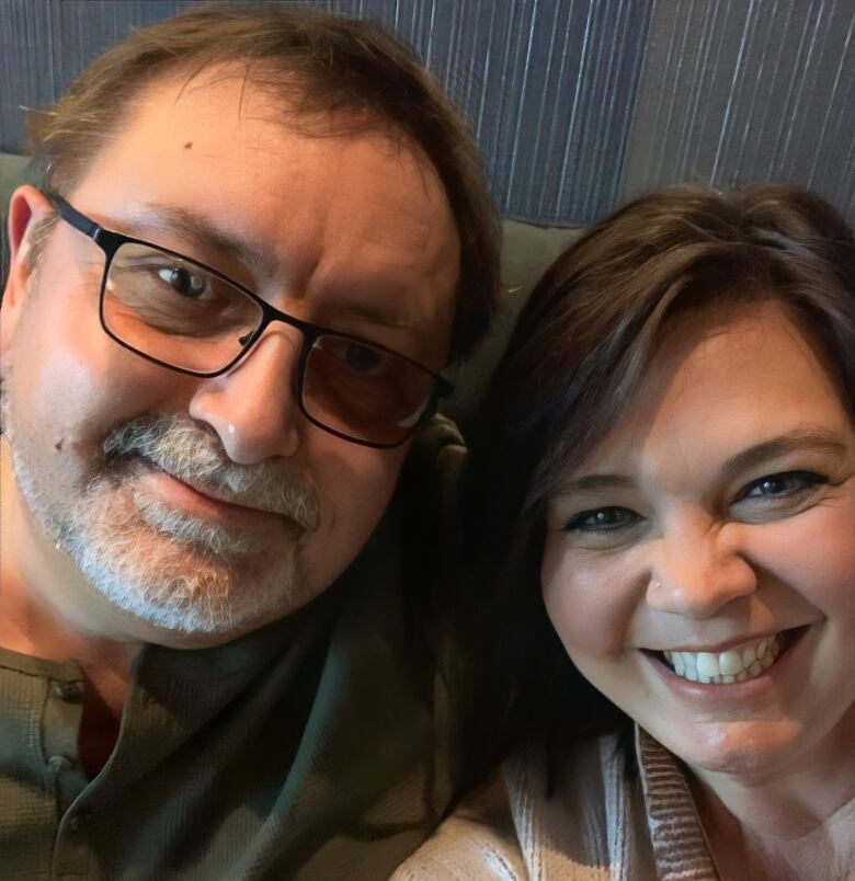 A man with glasses and a beard is shown in a selfie with a smiling woman.