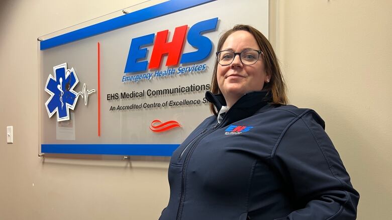 A woman wearing an Emergency Health Services jacket poses in front of an EHS sign. 