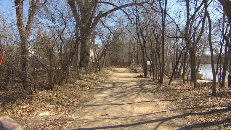 A gravel path runs through a treed area next to a river.