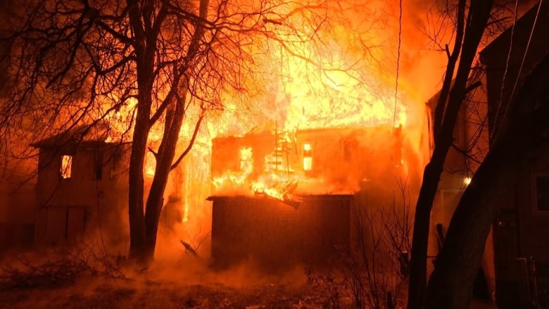 A photograph bathed in orange shows a large fire engulfing two buildings.