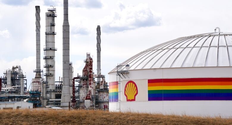 A large oil or fuel tank is shown in front of an industrial facility.