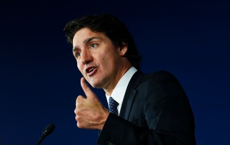 A man in a suit gestures while speaking into a microphone.