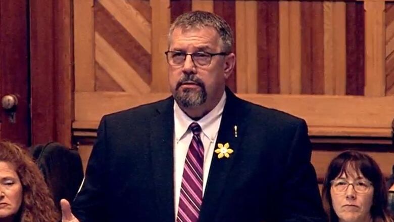 Screen shot of man in a suit speaking at a government gathering. 