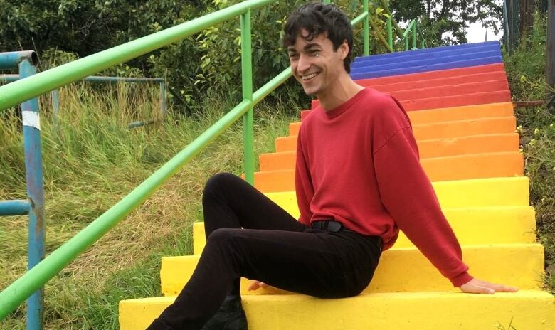 A young man sits on a set of rainbow steps. 