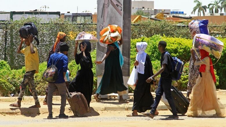 A line of people carrying bundles of their belongings above their heads. 