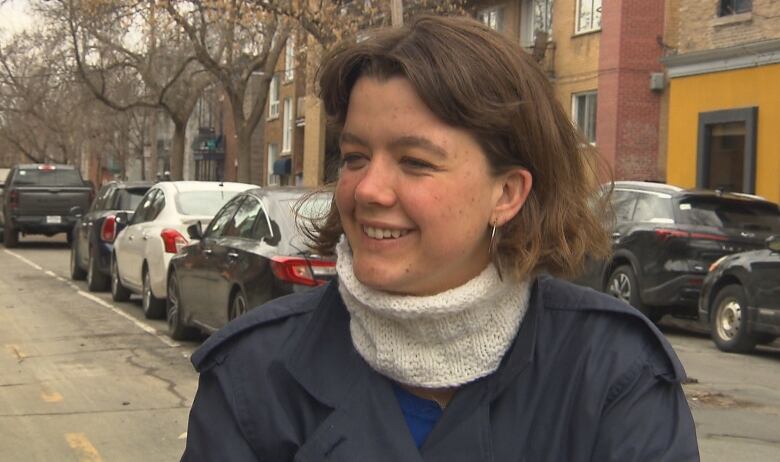 A woman with short hair and a neckwarmer on a bike path smiles into the camera. 