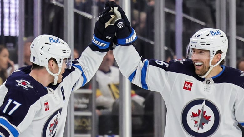 Two hockey players high-five each other in celebration as members of the audience watch on from the back.