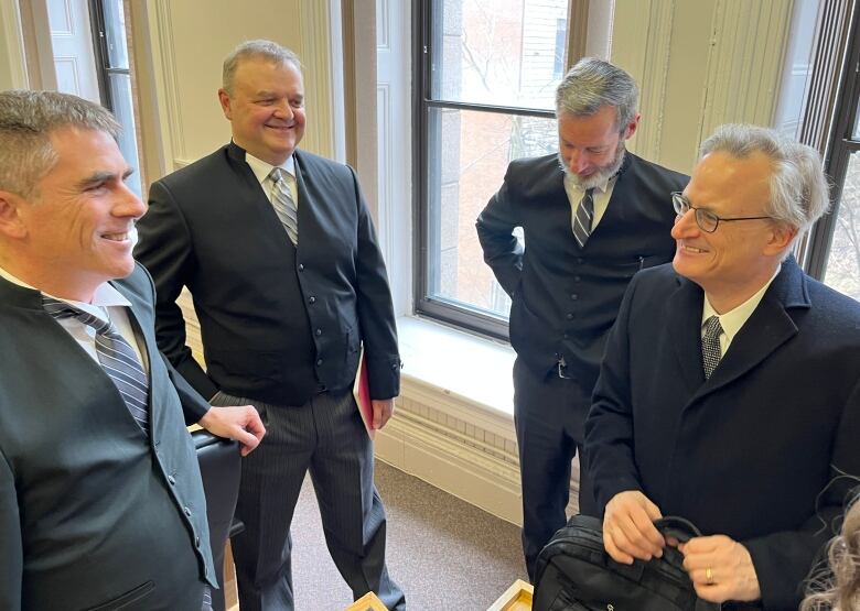 Four men in dark suits stand in a circle, talking.