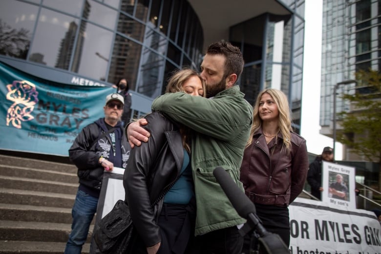 A blond woman is embraced by a man with short brown hair and a beard outside of a protest for Myles Gray.