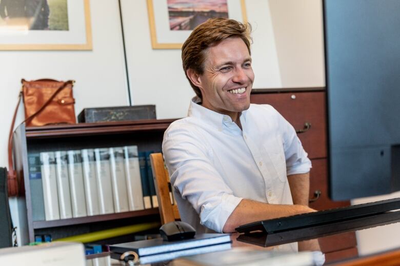 A smiling man sits at a desk. 