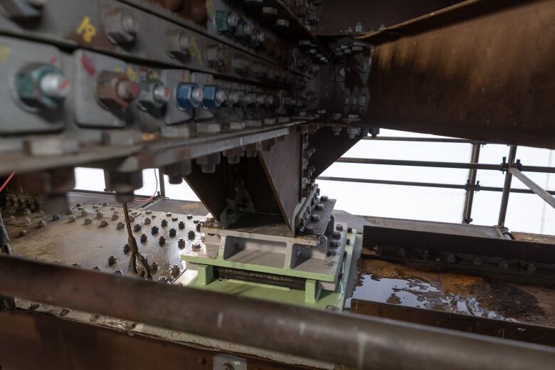 Metal supports with bolts on the underside of a bridge.