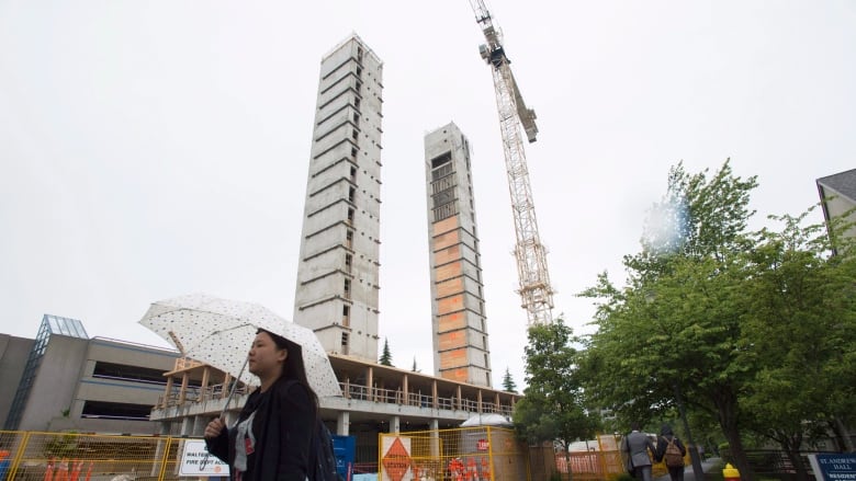 A woman with an umbrella walks past a construction site for two tower structures with a crane on an overcast day in Vancouver, B.C. 