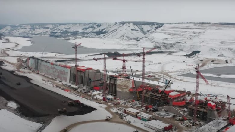 A snowy pipeline construction site near a river surrounded by hills in the middle of winter.