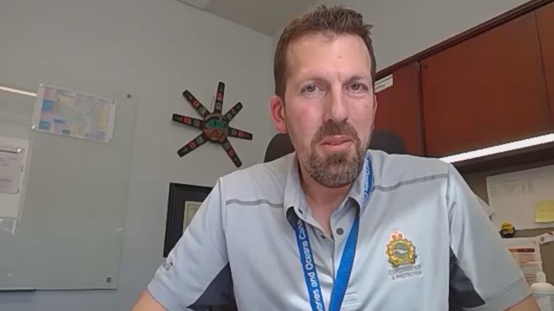 A man with short hair and facial hair wears a grey shirt with a blue lanyard.