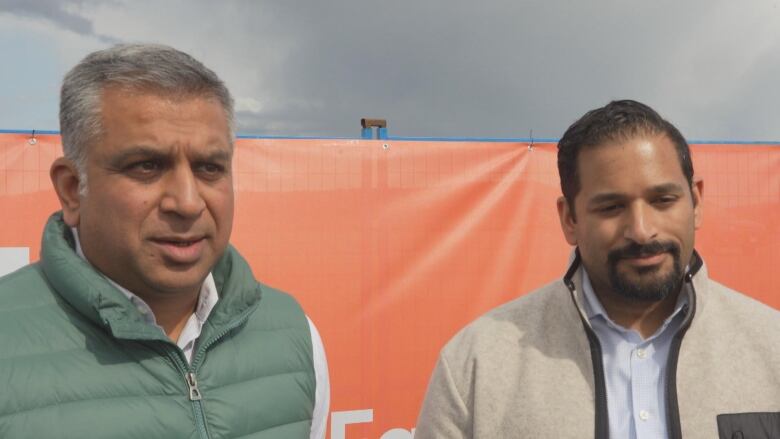 Two South Asian men stand in front of a construction hoarding.