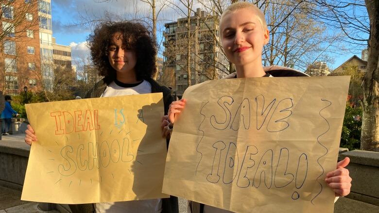 Two teenaged girls hold protest signs: one reads 