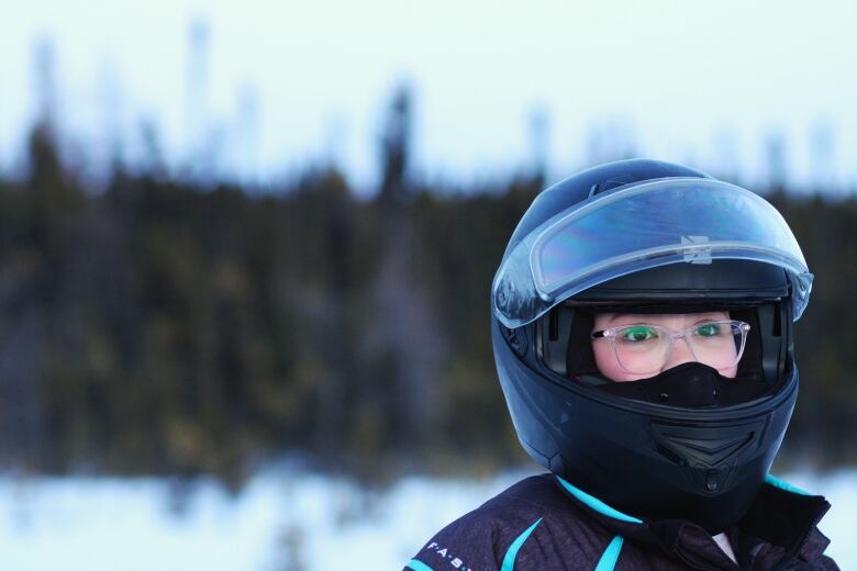 A young girl looks off into the distance while wearing a skidoo helmet. 