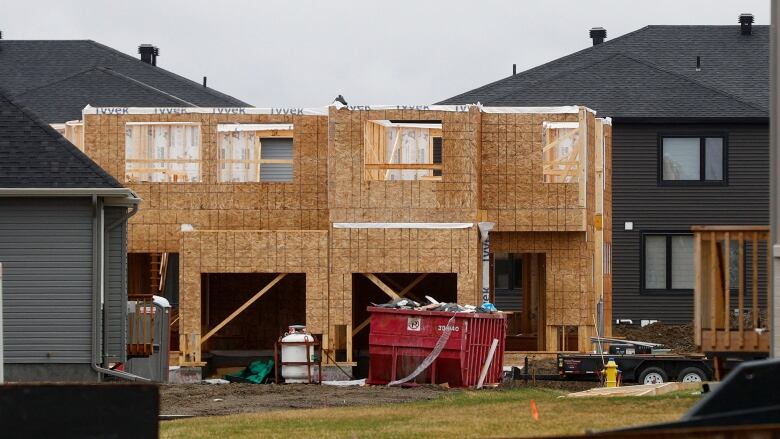 The wooden shell of a house under construction near homes that look finished, at least from the outside.