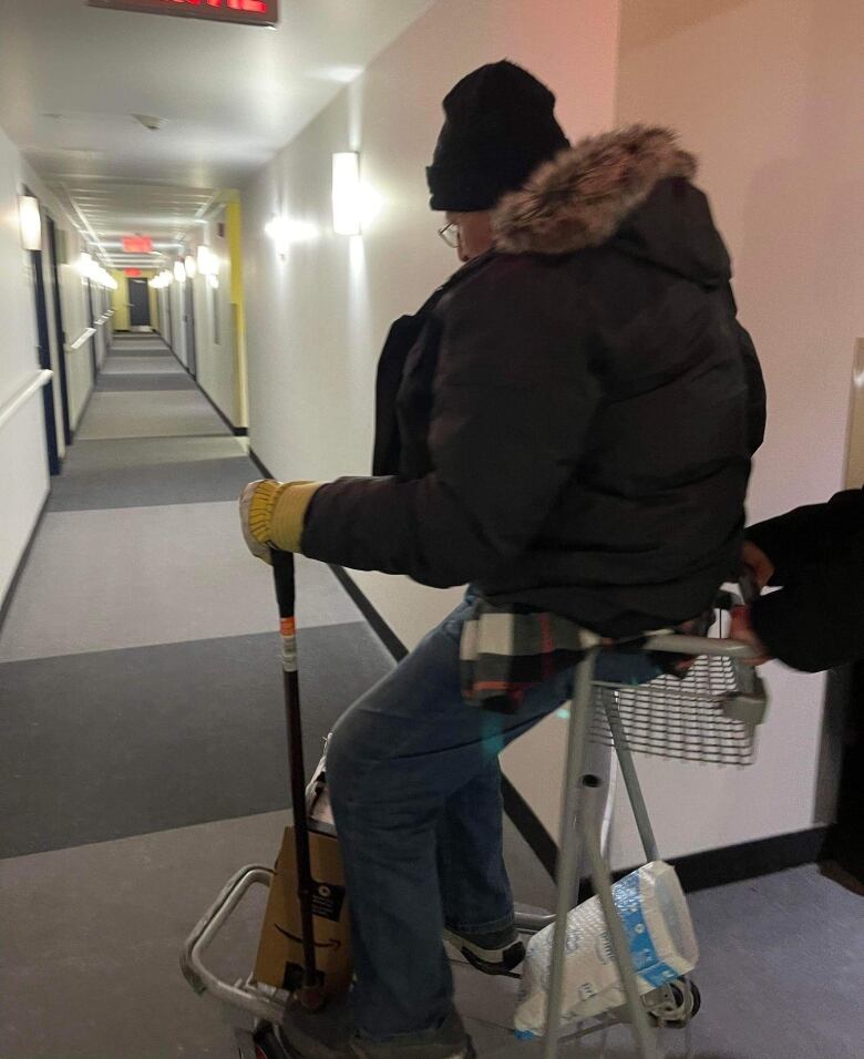 A man sits holding his cane in a luggage cart 