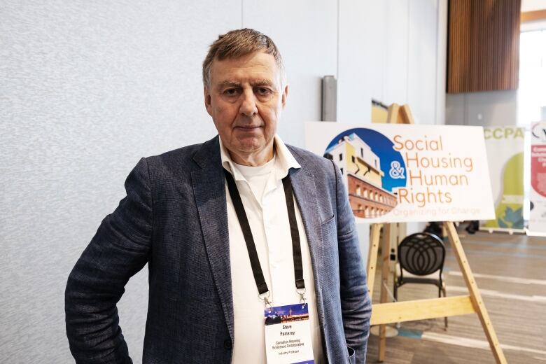 A man wearing a white shirt and blue suit jacket stands in front of a sign which reads Social Housing and Human Rights.