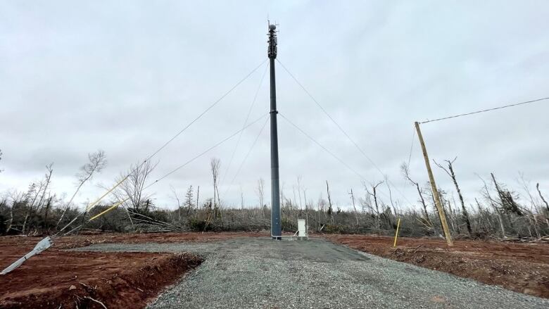 A tower stands amid a pad of gravel in a cleared field.