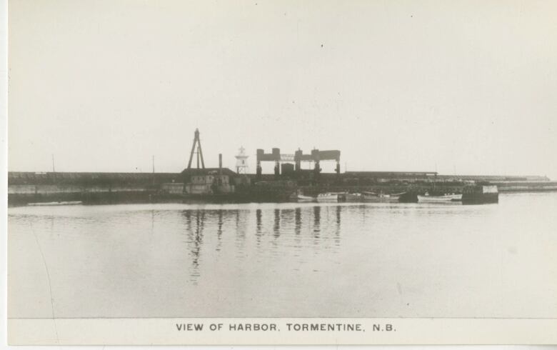 old black and white postcard showing view of harbour with lighthouse structure in distance