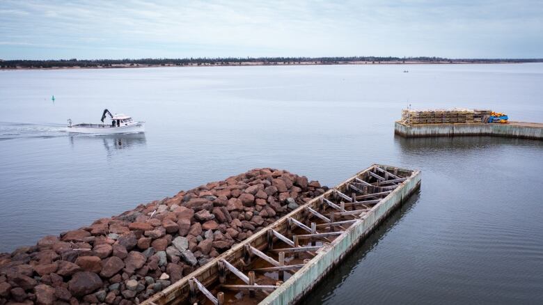 A fishing boat goees past a pile of rocks next to a wharf with no deck because of storm damage 