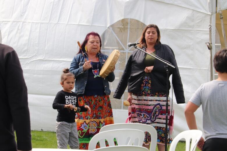 Indigenous singers with instruments. One is a child. 