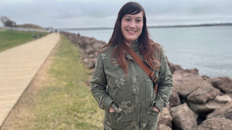 Jenn McCormick faces the camera at the boardwalk at Victoria Park with the Charlottetown Harbour behind her.