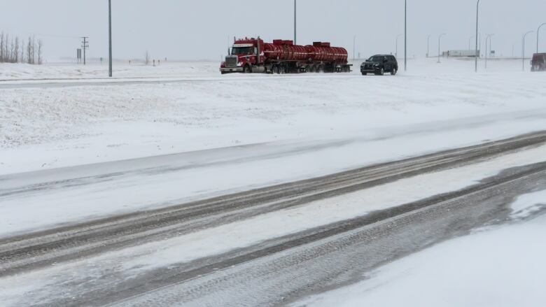 A red semi drives down a snow-covered stretch of highway.