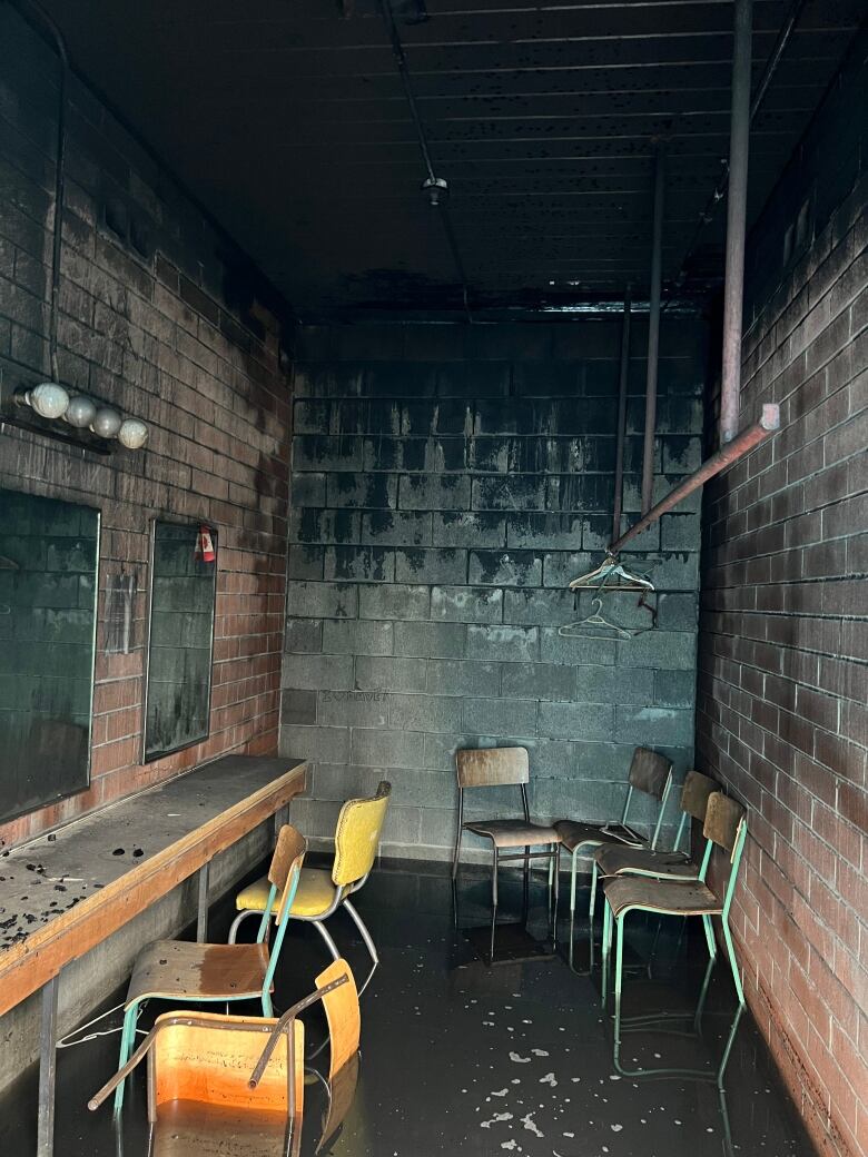 A flooded and charred green room, with chairs lying on the floor.