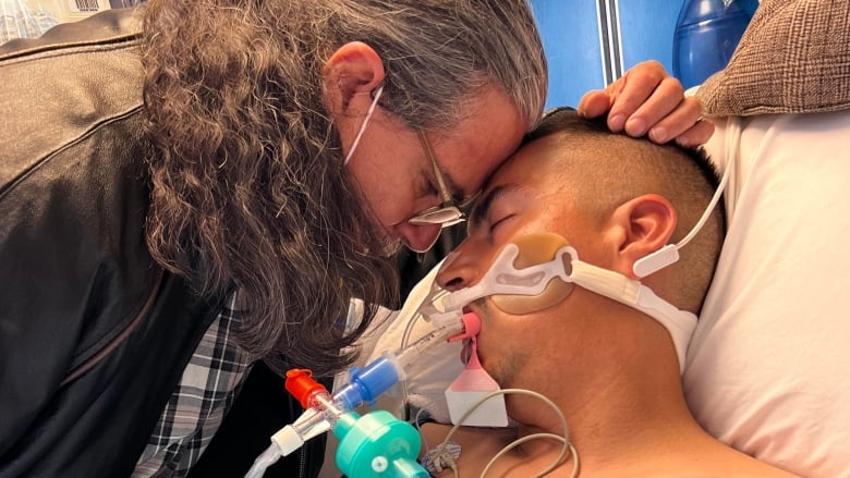 A father is pictured holding on to his son, who is on a ventilator.