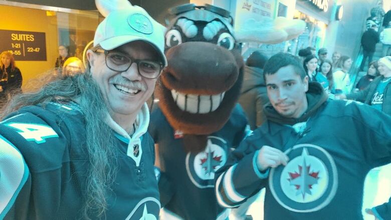 Two men are pictured in Winnipeg Jets jerseys, posing with a mascot.