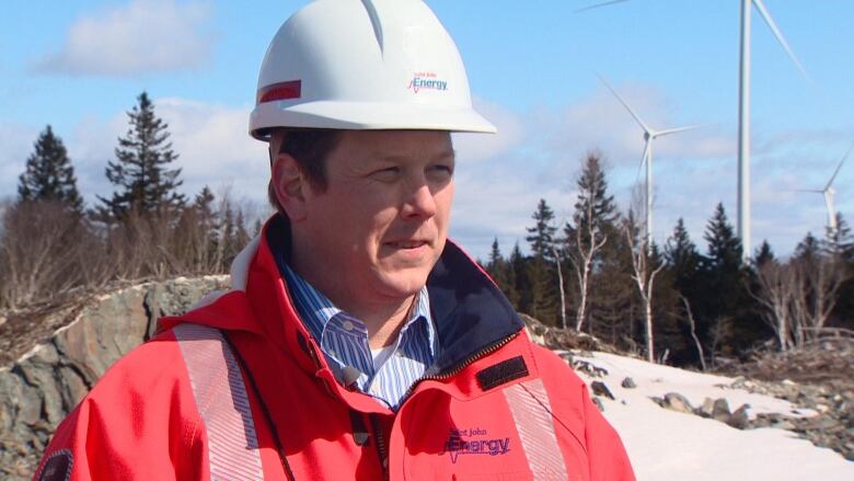 Andrew Ahearn wears construction helmet and stands in front of wind turbines.