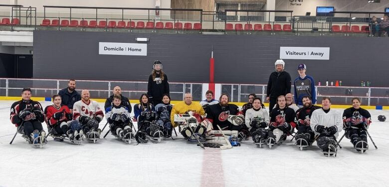 The New Brunswick para hockey team heading to nationals poses on the ice for a photo in their sleds. The team is lined up with three coaches standing behind. 