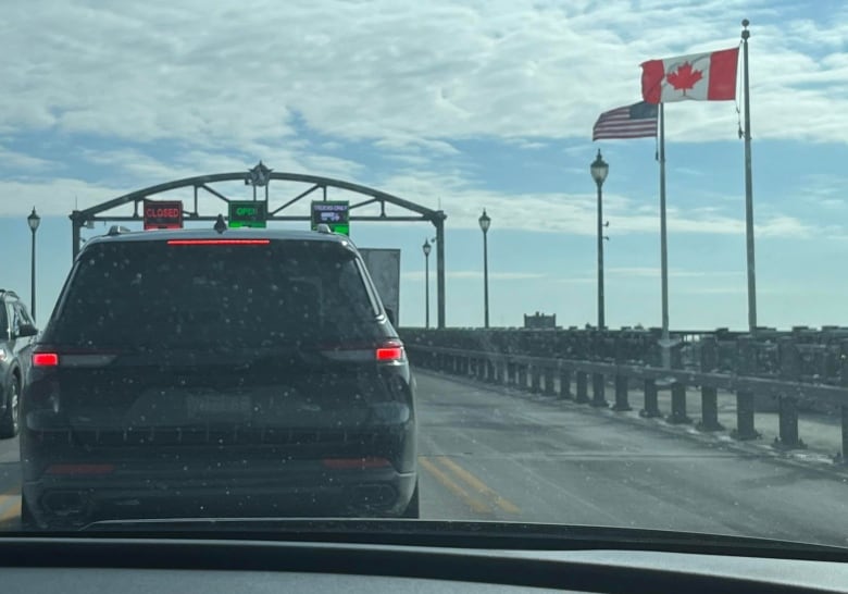 A vehicle on a bridge with a Canadian and American flag in the background.