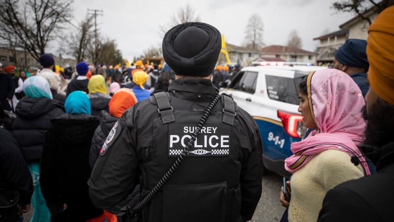 A police officer with the words 'Surrey Police' stands behind a procession of people.