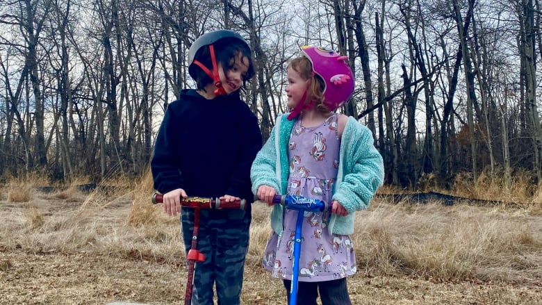 A boy and girl wearing bright coloured bike helmets smile at each other.