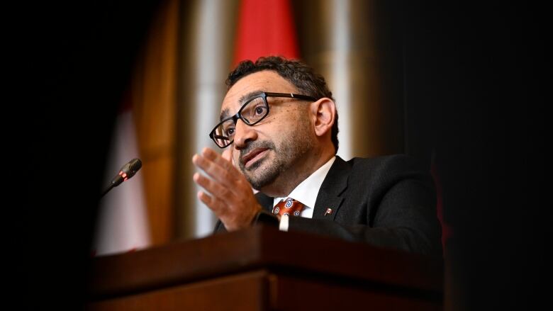 A man in a suit speaks at a podium.