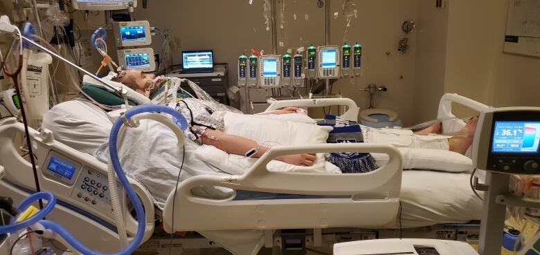 A teenager wearing a white gown with blue dots is pictured in a hospital bed with a neck brace and leads to multiple machines.